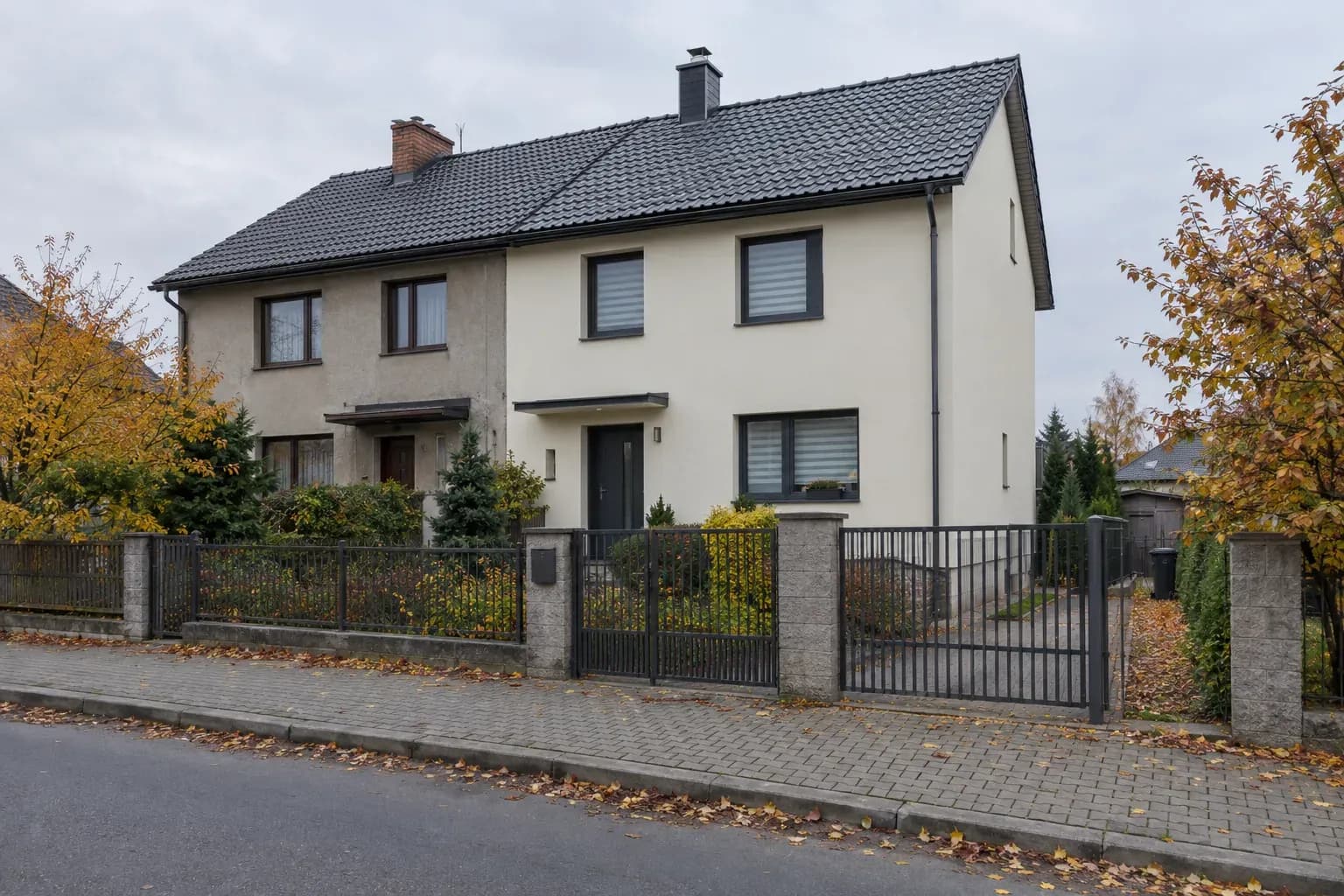 Dwa połączone domy jednorodzinne za ogrodzeniem, przy chodniku z kostki, jesienią